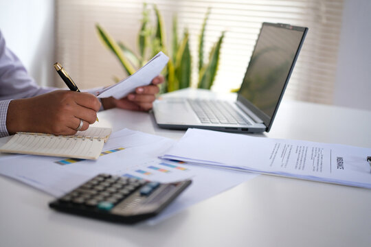 An accountant holds receipts or invoices, checks business documents, passbooks, bank statements, and calculates expenses paid via credit card before completing the bookkeeping.
