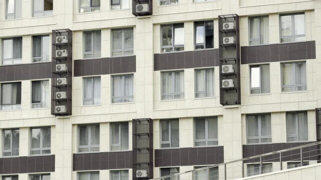 A modern apartment facade features repeating windows and metal-caged air conditioner units. The clean, geometric design creates a sense of stability, order, and calm in the urban environment.