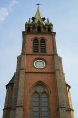 Obraz premium Low angle view of the historic red brick clock tower and green spire of Myeongdong Cathedral against a blue sky