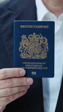 Closeup view of businessman hand holds British passport outdoor vertical shot. Male corporate employee demonstrates personal identification document of business travel. Citizenship