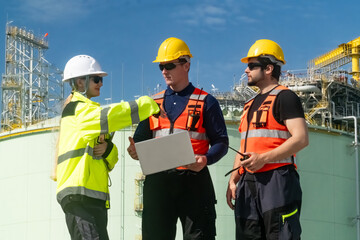 Fototapeta premium Workers discuss project at industrial site during daytime with machinery and storage tanks in background