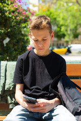 Obraz premium Teenager looking to his phone sitting on a bench outdoors