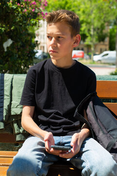Teenager looking to his phone sitting on a bench outdoors