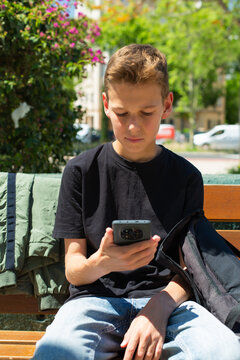Teenager looking to his phone sitting on a bench outdoors