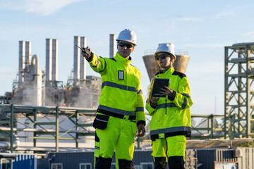 Fototapeta premium Workers discuss safety measures at an industrial site on a sunny day with equipment in the background