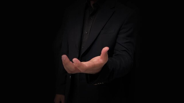 Man in black suit extending handshake in darkness symbolizing business partnership and trust