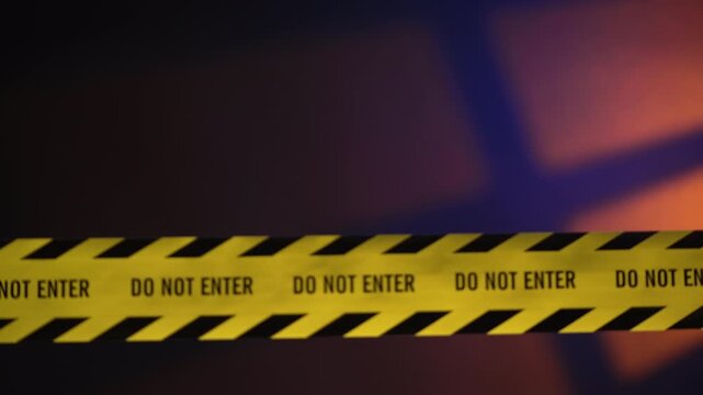 Yellow crime scene tape coming into focus revealing do not enter text with dramatic orange light and flashing sirens.