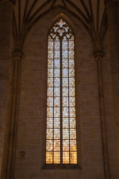 View of a tall Gothic stained glass window with intricate stone tracery and a grid pattern set in a historic stone wall in Freiburg im Breisgau, Baden-Wurttemberg, Germany.