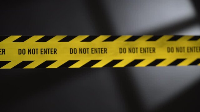 Focus pull from blur to sharp on do not enter text on yellow crime scene tape with flashing police lights and window shadow background.