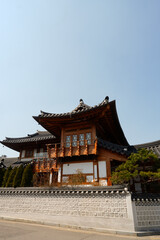 Fototapeta premium Traditional Korean hanok buildings with tiled roofs against a rocky mountain backdrop and clear blue sky