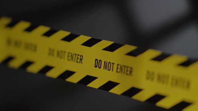 Focus shifting along do not enter text on yellow crime scene tape with flashing police lights and window shadow backdrop.