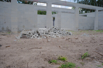 Unfinished cinderblock building at a residential construction site showing concrete block walls, exposed lintels, stacked lumber and gravel forecourt under a blue sky, illustrating building progress a © Del Harper
