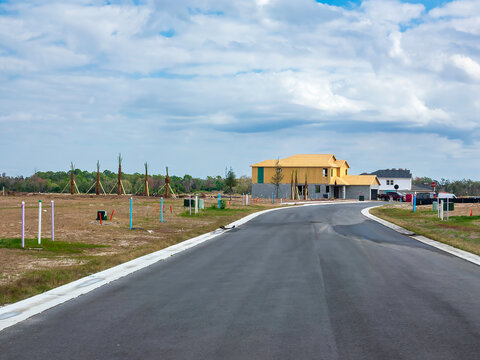 Two houses under construction along a curve in a new street with buildable lots marked on both sides in a suburban residential development in southwest Florida. Motifs of expansion and transformation.