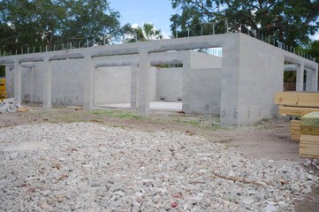 Unfinished cinderblock building at a residential construction site showing concrete block walls, exposed lintels, stacked lumber and gravel forecourt under a blue sky, illustrating building progress a © Del Harper
