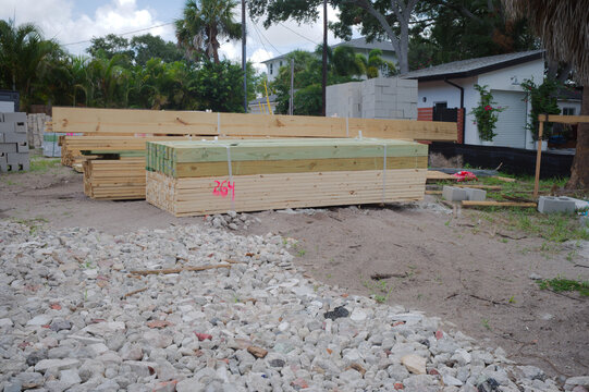 Unfinished cinderblock building at a residential construction site showing concrete block walls, exposed lintels, stacked lumber and gravel forecourt under a blue sky, illustrating building progress a