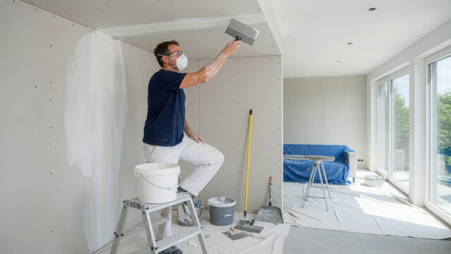 Man wearing protective mask applying joint compound to drywall ceiling in a generated using ai