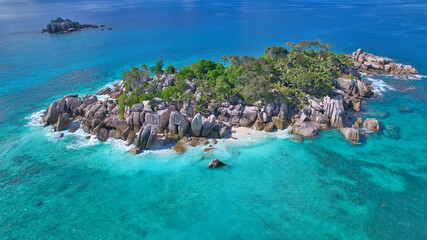 Stunning drone shot of Cocos Island, Seychelles, showing a luxury catamaran and boat anchored in clear turquoise water surrounded by granite rocks and coral reefs. © Nils