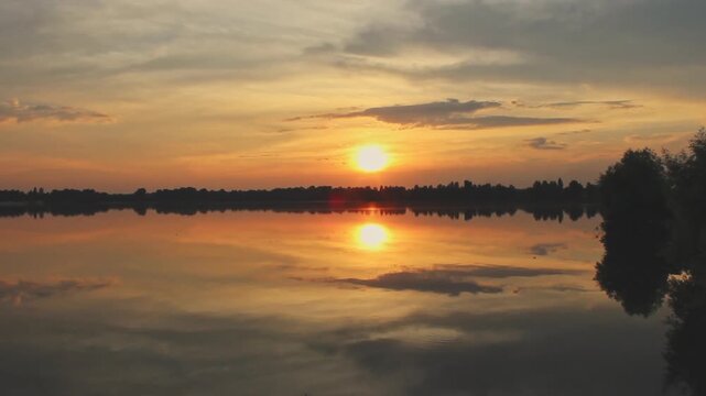 Beautiful sunset over a calm lake with golden reflections on the water surface. Colorful evening sky with clouds creating a peaceful natural landscape. Scenic lakeside view, tranquil atmosphere, and r
