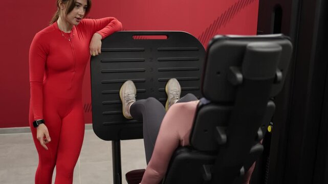 Female fitness trainer encourages a tired client to continue leg press repetitions despite low motivation demonstrating discipline persistence and workout coaching