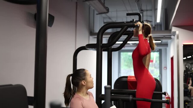 Personal trainer carefully observes client during assisted pull up exercise and records training results in notebook while tracking technique strength and progress