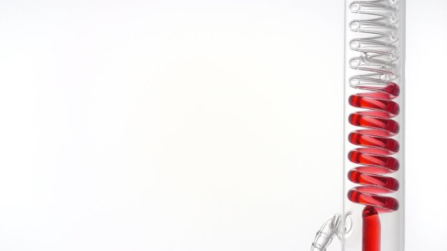 Red clean fluid flows through a vertically mounted coil lab condenser, visibly filling the coiled glass tube on the right side of the frame, leaving the left side as copy space with white background
