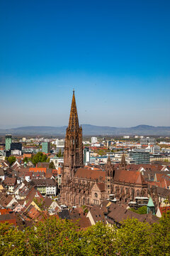 View of Freiburg Minster with its tall Gothic spire rising above the historic old town rooftops and surrounding hills Freiburg im Breisgau, Baden-Wurttemberg, Germany.