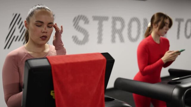 Women interrupt their cardio workout to check smartphones losing focus on fitness goals and becoming distracted by messages social media and digital notifications