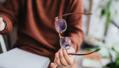 Fototapeta na wymiar Close-up of a person holding eyeglasses over a notebook on a desk. Casual office scene showing eyewear and hands during a business planning moment.