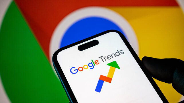 Closeup of a smartphone displaying the google trends logo with the google chrome browser icon in the background