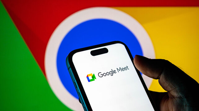 Closeup of a hand holding a smartphone displaying the google meet app logo against a google chrome browser background
