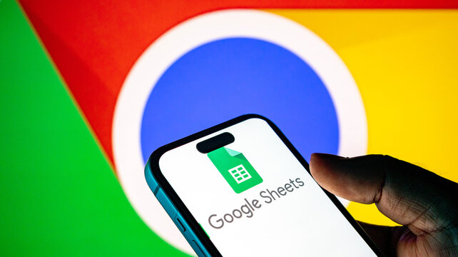 Person holding a smartphone displaying the google sheets app icon with a google chrome logo background