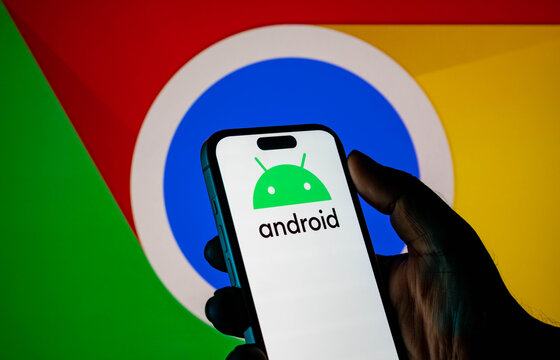 Hand holding a smartphone displaying the android logo with the google chrome logo in the background