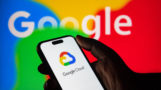 Hand holding a smartphone displaying the google cloud logo with a blurred google logo in the background