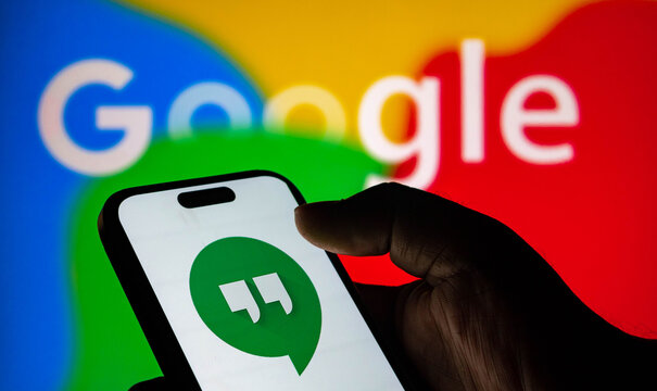 A person holding a smartphone displaying the google hangouts app logo in front of a google logo background