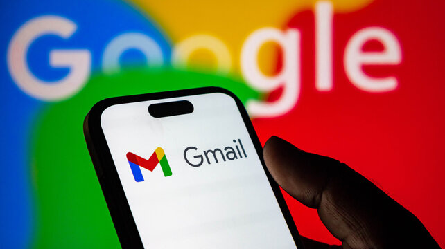 Hand holding a smartphone displaying the gmail logo with a blurred google logo in the background