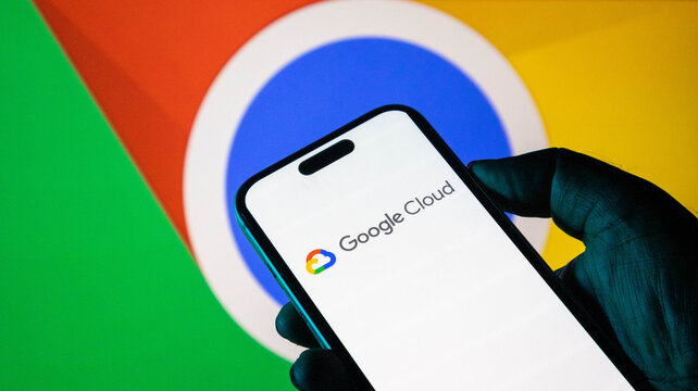 Hand holding a smartphone displaying the google cloud logo with the google chrome browser icon in the background