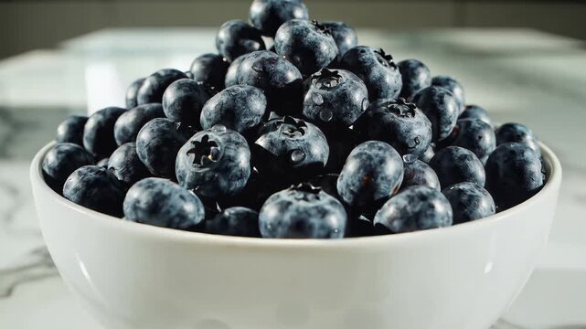 Heap of fresh blueberries in white bowl surrounded by loose berries on a textured surface