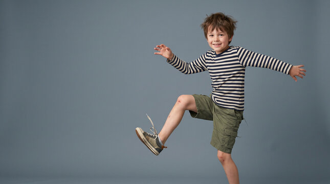 Energetic Boy Jumping with Scraped Knee in Striped Shirt on Grey Background