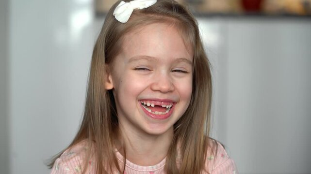 Portrait of happy toothless girl looks at camera and laughs. Close up of face of smiling child. Baby milk teeth change