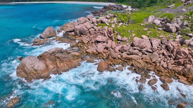 Breathtaking drone shot capturing the untamed beauty of Anse Cocos in Seychelles, showcasing clear turquoise ocean waves crashing against granite boulders and a remote white sand bay