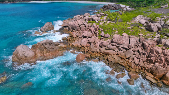Breathtaking drone shot capturing the untamed beauty of Anse Cocos in Seychelles, showcasing clear turquoise ocean waves crashing against granite boulders and a remote white sand bay