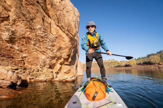 senior male is paddling stand up paddleboard along sandstone cliff on Horsetooth Reservoir in northern Colorado - POV