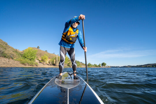 senior man paddling a stand up paddleboard on mountain lake - Horsetooth Reservoir , Colorado, in early fall scenery
