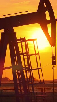 Silhouette of oil pump jack against a colorful beautiful sky with glowing clouds at sunset