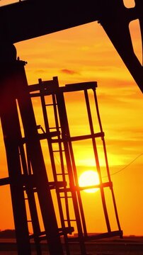 Silhouette of oil pump jack against a colorful beautiful sky with glowing clouds at sunset