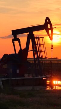 Silhouette of oil pump jack against a colorful beautiful sky with glowing clouds at sunset