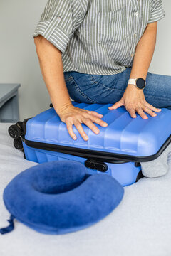 Woman closing overpacked suitcase with effort for travel