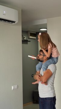 Father kept on shoulders little daughter and turn on air conditioner using remote control. Happy family adjust comfortable temperature of cooler system. Vertical shot