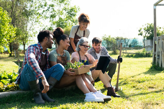 Diverse group of people discussing sustainable gardening using a digital tablet in a community garden