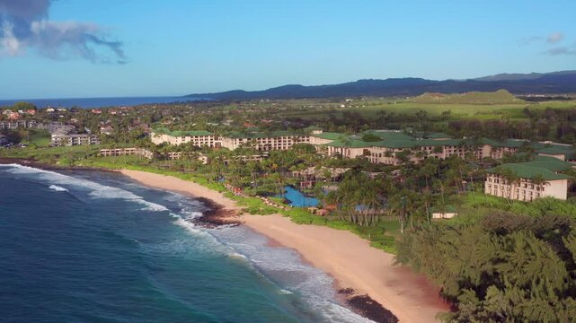 aerial view of a luxury beachfront resort in Kauai during a beautiful golden sunrise. drone footage captures the sprawling tropical hotel property, sandy beach coastline, and crashing ocean waves, fra